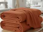 Zwei ordentlich gefaltete orangefarbene KraftKids Wandpaneel abgerundet Doppelkrepp-Stoffe liegen auf einem Holztisch mit Nähwerkzeugen und einem Maßband in der Nähe. Der sanft fokussierte Hintergrund schafft einen einladenden Raum für Wandgestaltungsprojekte.