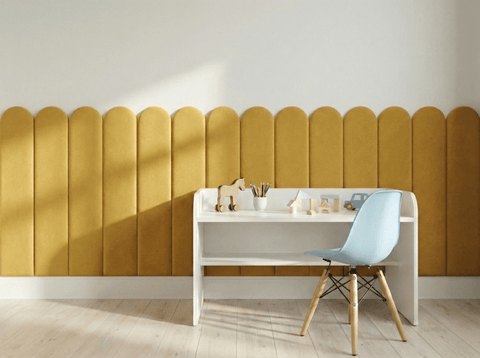 Ein minimalistisches Kinderzimmer mit einem kleinen weißen Schreibtisch, einem hellblauen Stuhl, Holzspielzeug und Buntstiften. An der Wand hängt der KraftKids Wandpaneel abgerundet Doppelkrepp in Senfgelb, der diesem modernen Raum eine gemütliche Note verleiht.