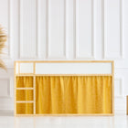 Ein modernes Kinderbett mit einem Rahmen aus Naturholz bietet KraftKids Hochbettvorhänge Set 2+1 in leinen gelb senfgelb für das Kura Bett, das vor einer weiß getäfelten Wand steht. In der Nähe bringen eine geflochtene Vase mit Pampasgras und zwei Holzhocker Charme auf den hellen Boden.