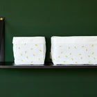 Zwei KraftKids Körbchen Musselin gelbe Zitronen mit gelben Zitronenmustern stehen auf einem schwarzen Regal vor einer dunkelgrünen Wand - ideal für Wickeltisch-Aufbewahrung. Das Regal hat eine schwarze Metallhalterung und eine goldene Schraube auf der linken Seite.