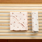 Zwei sauber gefaltete KraftKids Musselin Babydecken für Babyschale, eine quadratische und eine rechteckige mit Kirschenmuster, liegen nebeneinander auf leichten Holzlatten - perfekt als leichte Sommerdecken für Ihr Baby.