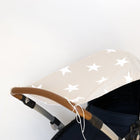 Eine Nahaufnahme des KraftKids Sonnensegels große weiße Sterne auf Beige, ein Kinderwagen-Sonnenschirm mit großen weißen Sternen auf Beige, der an einem braunen und silbernen Griff vor einem schlichten weißen Hintergrund befestigt ist.