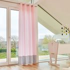 Ein helles Kinderzimmer mit großen Fenstern, die mit "Gardinen kleine Blätter rosa auf Weiß" von KraftKids verkleidet sind, hellen Holzböden, einer weißen Wiege unter einer schrägen Decke mit einem Mobile und Blick auf Bäume und Häuser draußen.