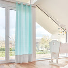 Ein helles, modernes Zimmer mit großen Fenstern, hellen Holzböden und KraftKids Gardinen "weiße Pfeile auf Mint Unigrau" aus 100% Baumwolle. Enthält einen kleinen weißen Schreibtisch und einen Stuhl sowie ein hängendes Wolkenmobile mit bunten Regentropfen.