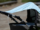 Nahaufnahme eines Kinderwagens mit dem KraftKids Sonnensegel "weiße Pfeile auf Blau" als Schattenspender drapiert. Perfekt für optimalen Sonnenschutz des Babys beim Spaziergang im Freien an einem sonnigen Tag.