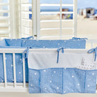 Ein weißes Kinderbett mit der KraftKids Betttasche abgerundete Dreiecke weiß auf Blau hängt in der Nähe, blaue Bettwäsche mit weißen geometrischen Mustern neben großen Fenstern in einem handgefertigten Kinderzimmer, Sonnenlicht strömt herein und gibt den Blick auf einen Sandstrand frei.