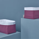 Zwei handgenähte KraftKids Körbchen Musselin purpur mit weißen Tops und lila Basen stehen auf hellblauen Podesten vor einer blauen Wand - ideal zur Aufbewahrung am Wickeltisch.