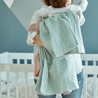 Eine Frau hält ihr Baby kuschelig eingewickelt in die weiche KraftKids Babydecke Musselin mint Pusteblumen.