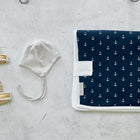 Ein Paar hellbraune Babyschuhe, eine grau gestreifte Mütze und die Reisewickelunterlage Musselin dunkelblau Anker mit Ankeraufdruck von KraftKids liegen auf einer hellgrauen Unterlage - die perfekten Utensilien für Ausflüge mit Ihrem Kleinen.