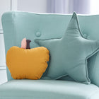 Im Kinderzimmer steht ein hellblauer Polsterstuhl mit einem gelben Apfelkissen und dem KraftKids Sternkissen Musselin nilblau, daneben eine weiße Kommode mit schwarzen Knöpfen.