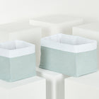 Zwei grüne Körbchen Musselin mit goldenen Punkten von KraftKids stehen auf weißen Podesten vor weißem Hintergrund - stilvolle und praktische Aufbewahrung.