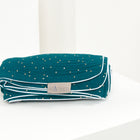 Eine gefaltete KraftKids Babydecke Musselin goldene Punkte auf Petrol mit weißem Rand und kleinen goldenen Punkten, die ein KraftKids-Etikett tragen, wird auf einer weißen Fläche vor einem neutralen Hintergrund platziert.