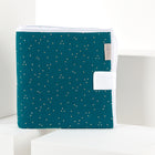 Eine gefaltete KraftKids Reisewickelunterlage Musselin mit goldenen Punkten auf Petrol steht auf weißer Fläche, mit Stoffetikett und Ecke-ideal als platzsparende Wickelauflage oder praktische Reiseauflage für unterwegs.