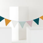 Die KraftKids Wimpelkette goldene Punkte auf Musselin in den Farben Teal, Senfgelb, Rosa, Hellblau und Weiß mit goldenen Punkten ziert weiße geometrische Blöcke im minimalistischen Kinderzimmer-Deko-Stil.