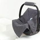 Ein dunkelgrauer Autositz mit Griff, der mit einem Drei-Punkte-Gurt-System ausgestattet ist, wird mit der KraftKids Babydecke für Babyschale Sommer Musselin in Grau mit goldenen Punkten drapiert und ruht auf weißen, treppenartigen Plattformen vor einem schlichten Hintergrund.