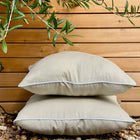 Zwei KraftKids Kissenbezug Leinen Natur Braun im Außenbereich mit einem belaubten Baum und einer Holzlattenwand, die auf kleinen Felsen stehen - eine ideale Ergänzung für Ihre Bettwäschekollektion.