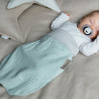 Ein schlafendes Baby mit Schnuller ruht friedlich im KraftKids Strampelsack Herbst Winter Musselin goldene Punkte auf Grün, umgeben von beigen sternförmigen Kissen, und macht es sich in dem weichen, stylischen Schlafsack gemütlich.