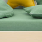 Nahaufnahme eines ordentlich gemachten Bettes mit dem KraftKids Spannbettlaken Doppelkrepp Grün Jade, zwei grünen Kissen und einem gelben sternförmigen Kissen. Das Bettgestell aus hellem Holz ist die perfekte Ergänzung zu dieser Kinderbettwäsche.