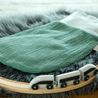 Der KraftKids Strampelsack Frühling Sommer Doppelkrepp Grün Jade ruht auf einer flauschigen grauen Matte, umgeben von einer hölzernen Spielzeugeisenbahn mit einem weißen Spielzeugeisenbahnzug.