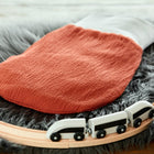 Ein KraftKids Strampelsack Frühling Sommer Doppelkrepp Rot Herbstrot Babyschlafsack liegt auf einem grauen Plüschteppich, mit einer hölzernen Spielzeugeisenbahnschiene und einem weißen Spielzeugeisenbahn im Vordergrund.