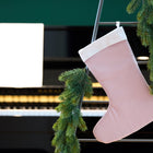 Eine KraftKids Weihnachtssocke Doppelkrepp Rosa hängt an einer Leiter mit grüner Tannengirlande, während im Hintergrund ein Klavier und leere Notenblätter zu sehen sind.