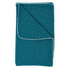 Die KraftKids Babydecke Musselin goldene Punkte auf Petrol ist eine gefaltete blaugrüne Decke mit kleinen goldenen Punkten und weißer Paspelierung entlang der Ränder, abgebildet auf einem weißen Hintergrund.