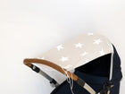 Eine Nahaufnahme des KraftKids Sonnensegels große weiße Sterne auf Beige mit einem beigen Verdeck mit großen weißen Sternen auf einem Kinderwagen mit braunem Griff hebt sich von einem schlichten weißen Hintergrund ab.