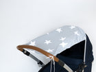 Der KraftKids Sonnensegel große weiße Sterne auf Grau ist ein hellgraues Kinderwagenverdeck mit großen weißen Sternen, hergestellt aus atmungsaktiver Baumwolle. Abgebildet auf einem Kinderwagen mit braunem Griff und dunkelmarinefarbenem Sitz vor einem schlichten weißen Hintergrund.