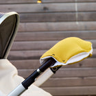 Eine Nahaufnahme eines Kinderwagengriffs mit dem KraftKids Kinderwagenmuff Doppelkrepp Gelb Senf, handgenäht aus gelbem Vlies. Ebenfalls zu sehen sind das Verdeck des Kinderwagens, ein Teil einer cremefarbenen Decke und ein Holzzaun im Hintergrund.