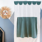 Das KraftKids Puppentheater Kasperletheater Doppelkrepp Grün Jade inkl.. Teleskopstange mit grünem Wellenschliff hängt an einer geometrischen Wand, daneben ein runder Strohlöwe als Dekoration und eine Kreidetafel mit Zeichnungen in der Ecke.