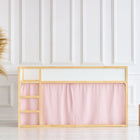Ein minimalistisches Zimmer mit einem KraftKids Hochbettvorhänge Set 2+1 Musselin goldene Punkte auf Rosa für das Kura Bett, einem Holzrahmen, einem rosa Vorhang, einer hohen Korbvase mit Pampasgras und zwei Holzhockern vor einer weiß getäfelten Wand.