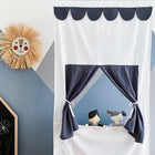 Das KraftKids Puppentheater Kasperletheater Musselin goldene Punkte auf Grau inkl. Teleskopstange ist an einer Wand mit geometrischen Formen ausgestellt, neben einer Kreidetafel mit bunten Zeichnungen und einem dekorativen Strohlöwengesicht.